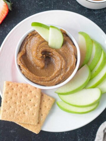 Bowl of healthy cookie butter on a plate with sliced apples and graham crackers.