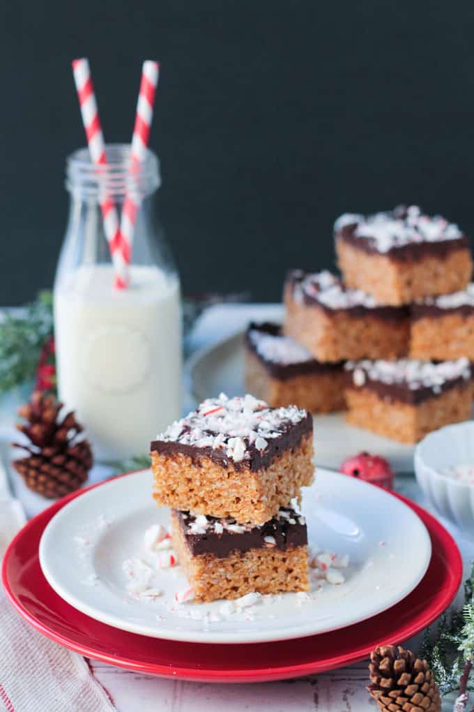 Plateful of rice krispie treats next to a bottle of milk. In front a plate with two stacked crispy bars.