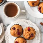 Three pumpkin cranberry muffins on a white plate in front of a cup of coffee.