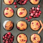 Baked muffins in a muffin pan with fresh cranberries filling some of the cavities.