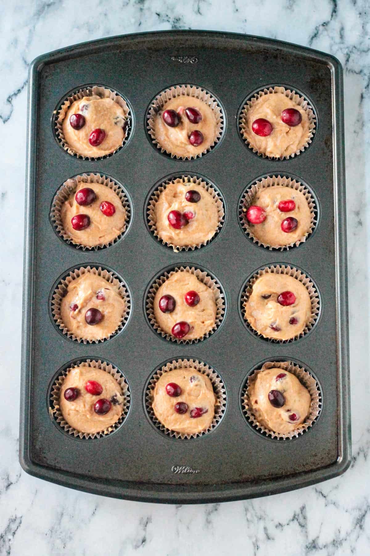 Fresh cranberries dotted on top of the muffin batter in the cupcake tin.