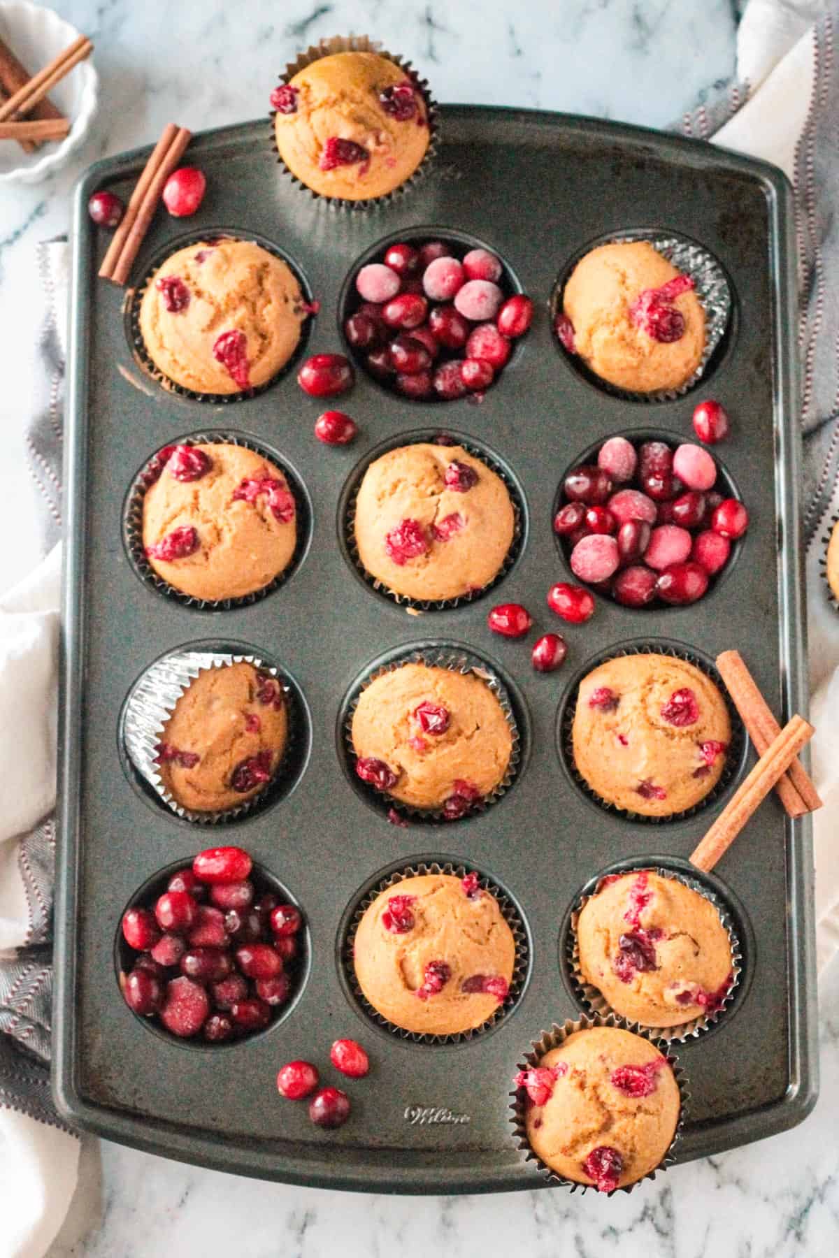 Baked pumpkin cranberry muffins in a muffin pan with fresh cranberries filling some of the cavities.