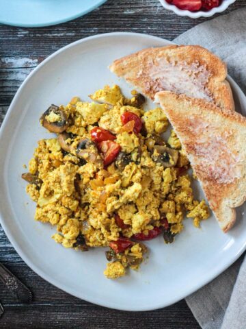 Tofu veggie scramble on a plate with two pieces of buttered toast.