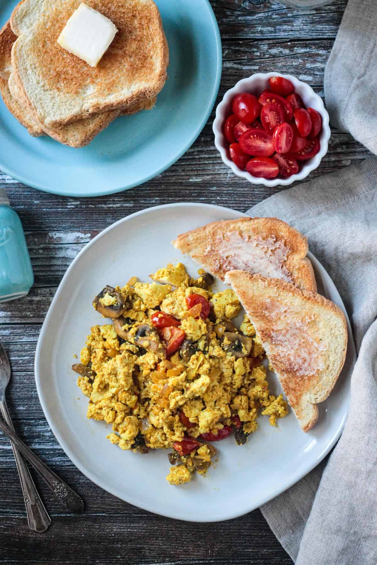 Tofu veggie scramble on a plate with two pieces of buttered toast.