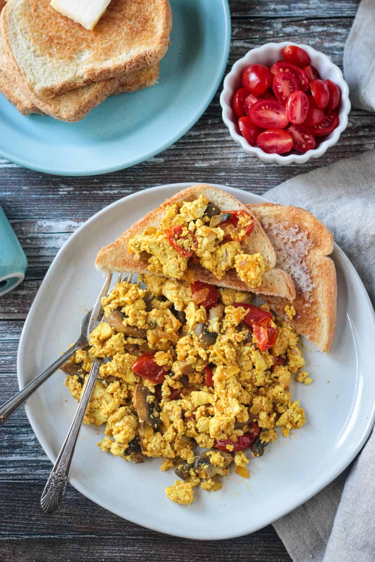 Two forks on a plate with vegan scrambled eggs and toast.