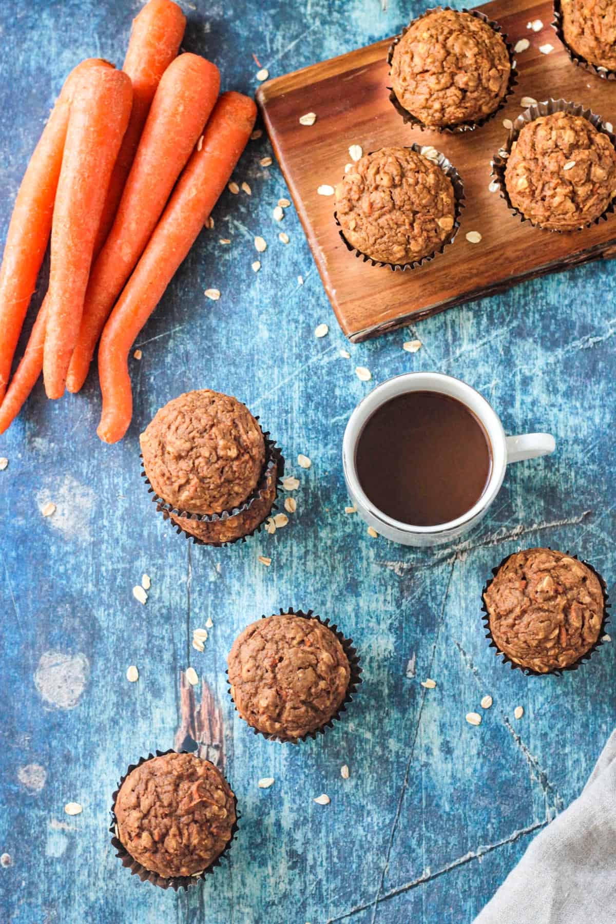 Several baked muffins lying on a blue background with a cup of coffee.