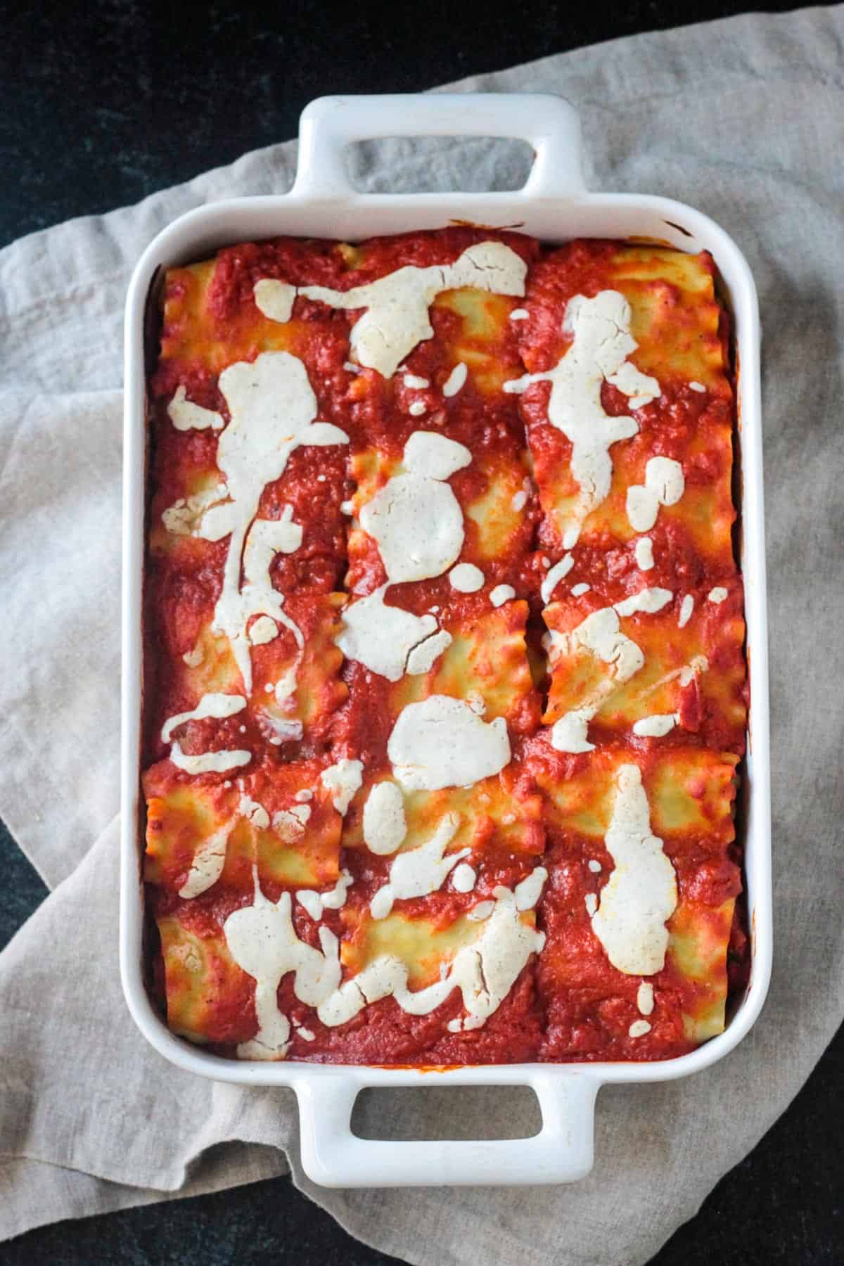 Full pan of lasagna roll ups covered in marinara and drizzled with white sauce.