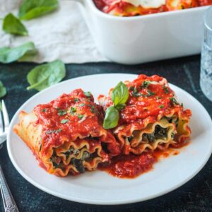 Two lasagna roll ups on a white plate garnished with fresh basil.