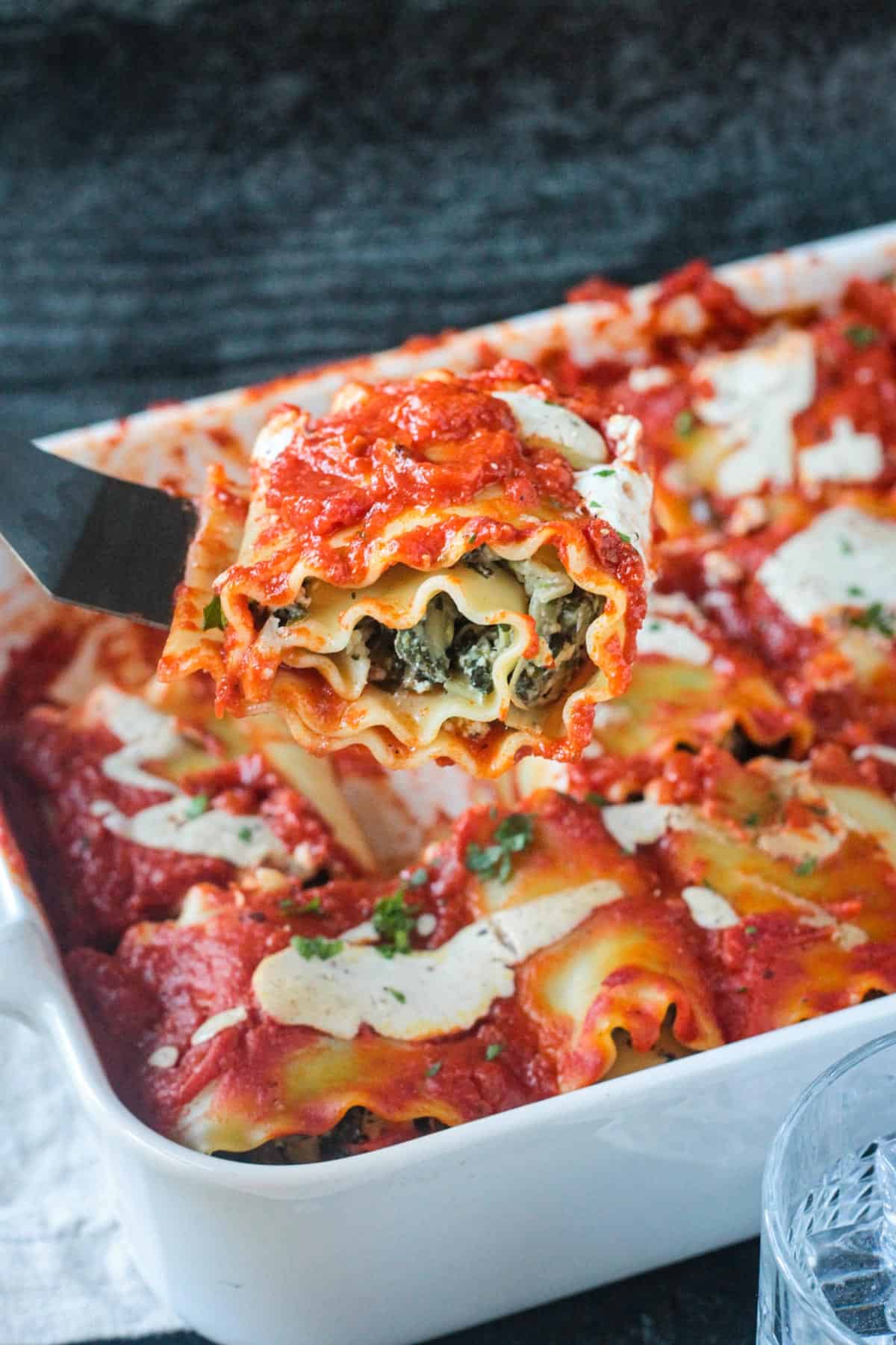 Spatula lifting one spinach pasta roll out of a baking dish.