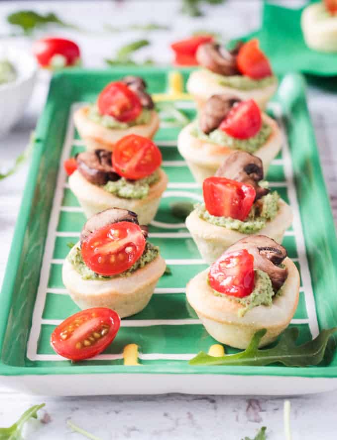 Tray of vegan pizza bites topped with pesto, cherry tomatoes, and mushrooms.