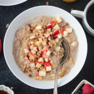 A bowl of whole grain porridge topped with apples.