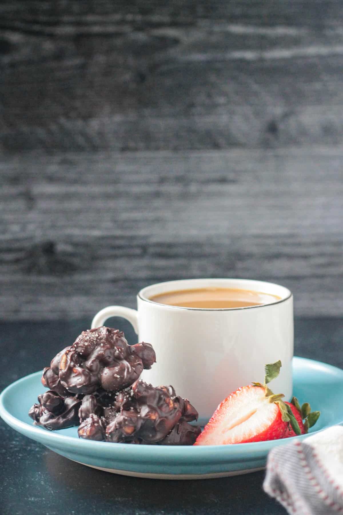 Several nut clusters on a blue plate with a cup of coffee and one strawberry.