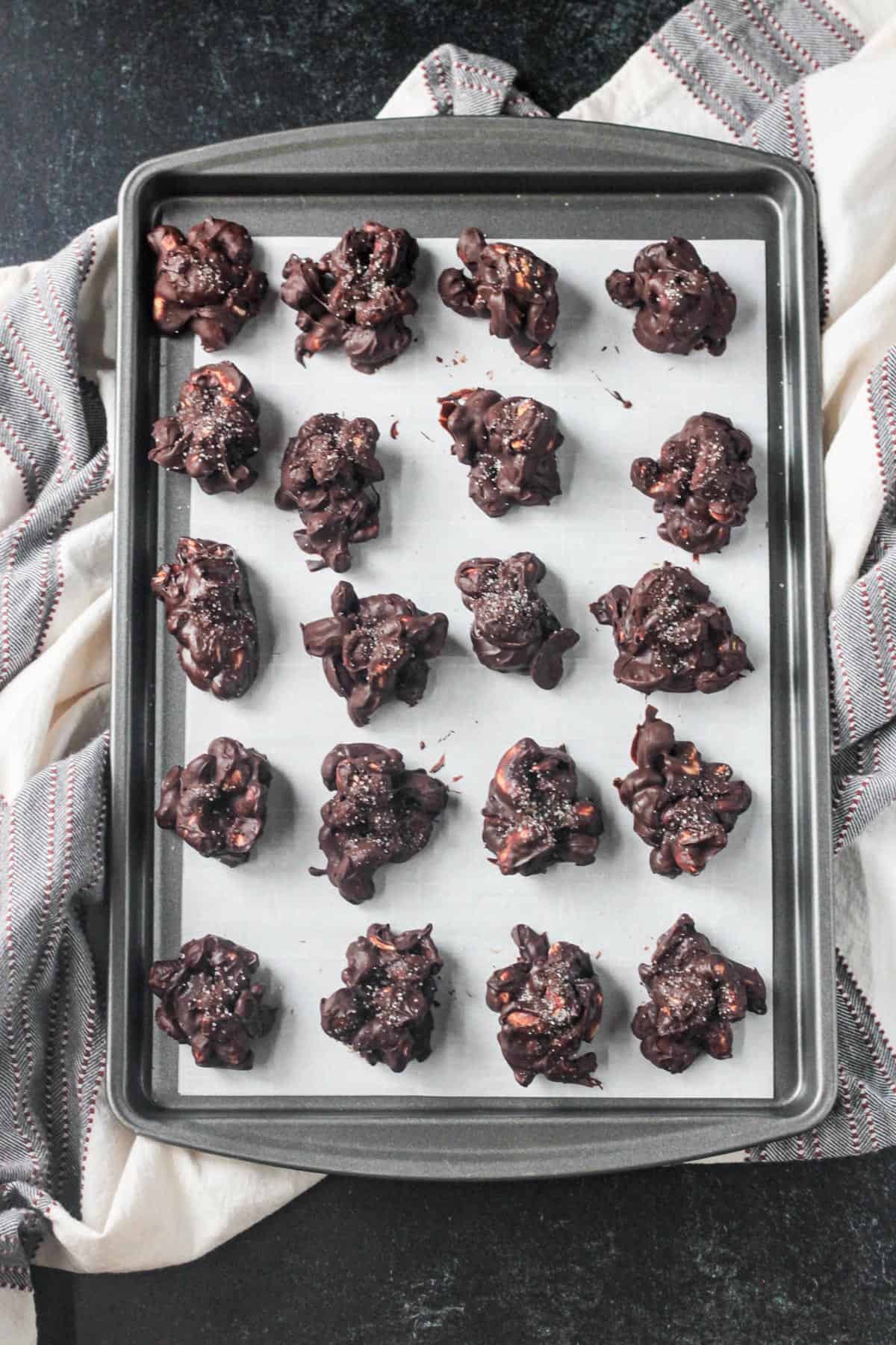Tray of chocolate covered cashew clusters on parchment paper.
