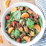 Lentil Quinoa Salad in a white bowl next to a striped dish towel and slices of orange.