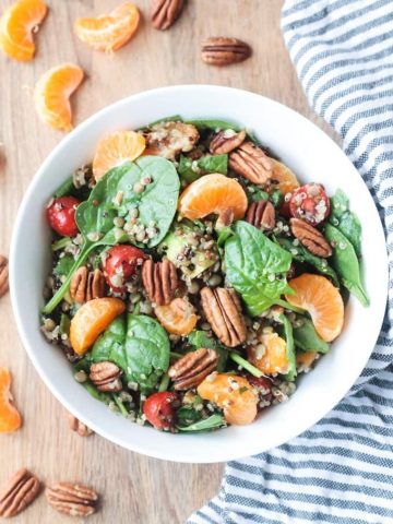 Lentil Quinoa Salad in a white bowl next to a striped dish towel and slices of orange.