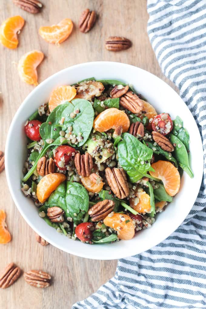 Lentil Quinoa Salad in a white bowl next to a striped dish towel and slices of orange.