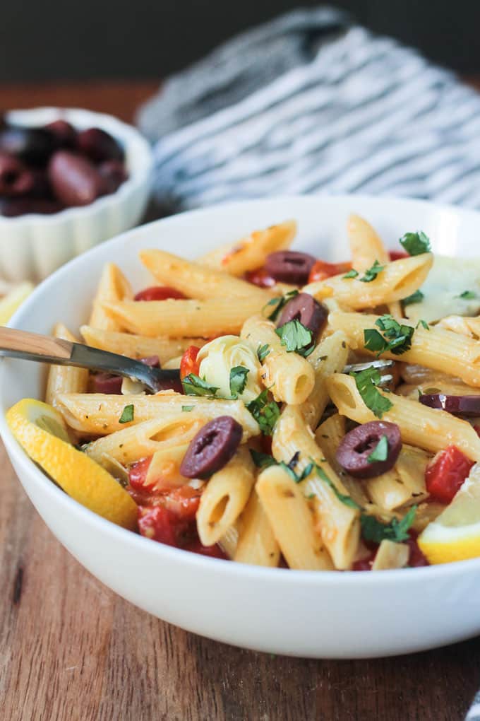 A wooden handled metal fork in a bowl of Mediterranean Pasta & veggies.