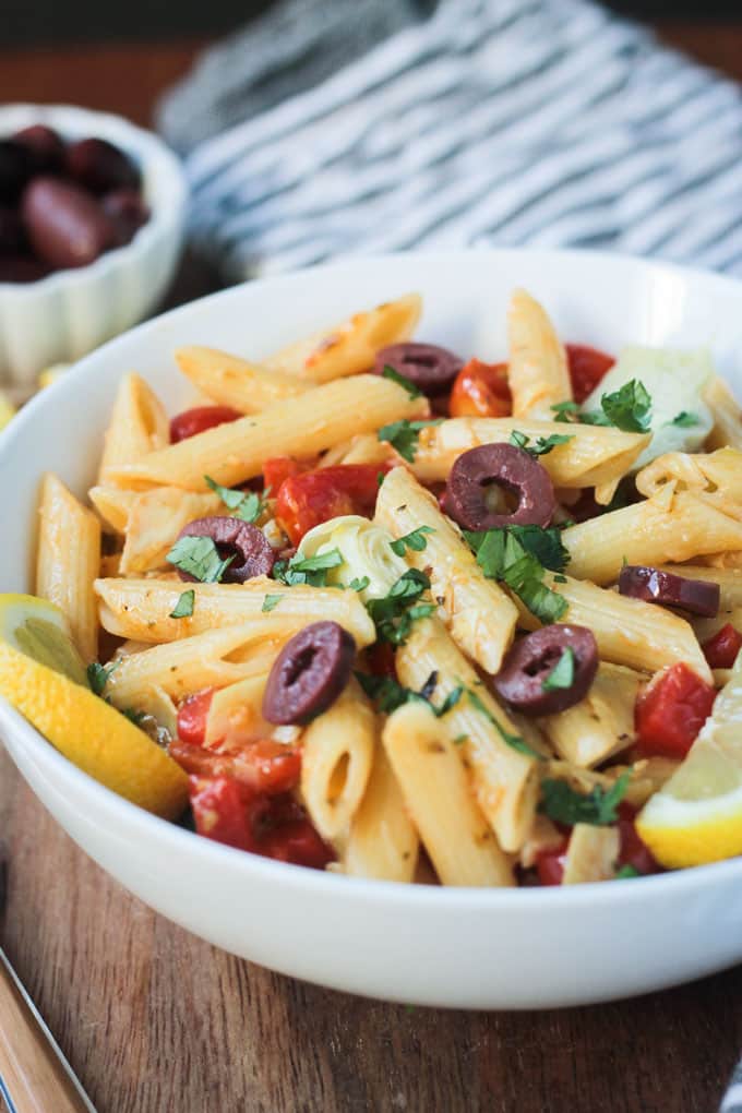 Bowl of penne pasta, peppers, tomatoes, artichokes, and olives. 