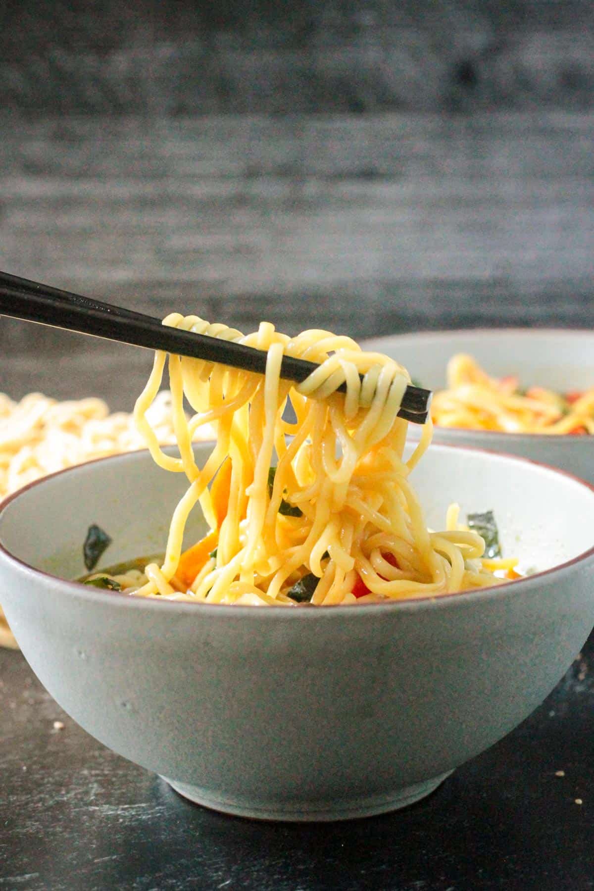 Chopsticks pulling noodles out of a bowl of spicy vegan ramen noodle soup.