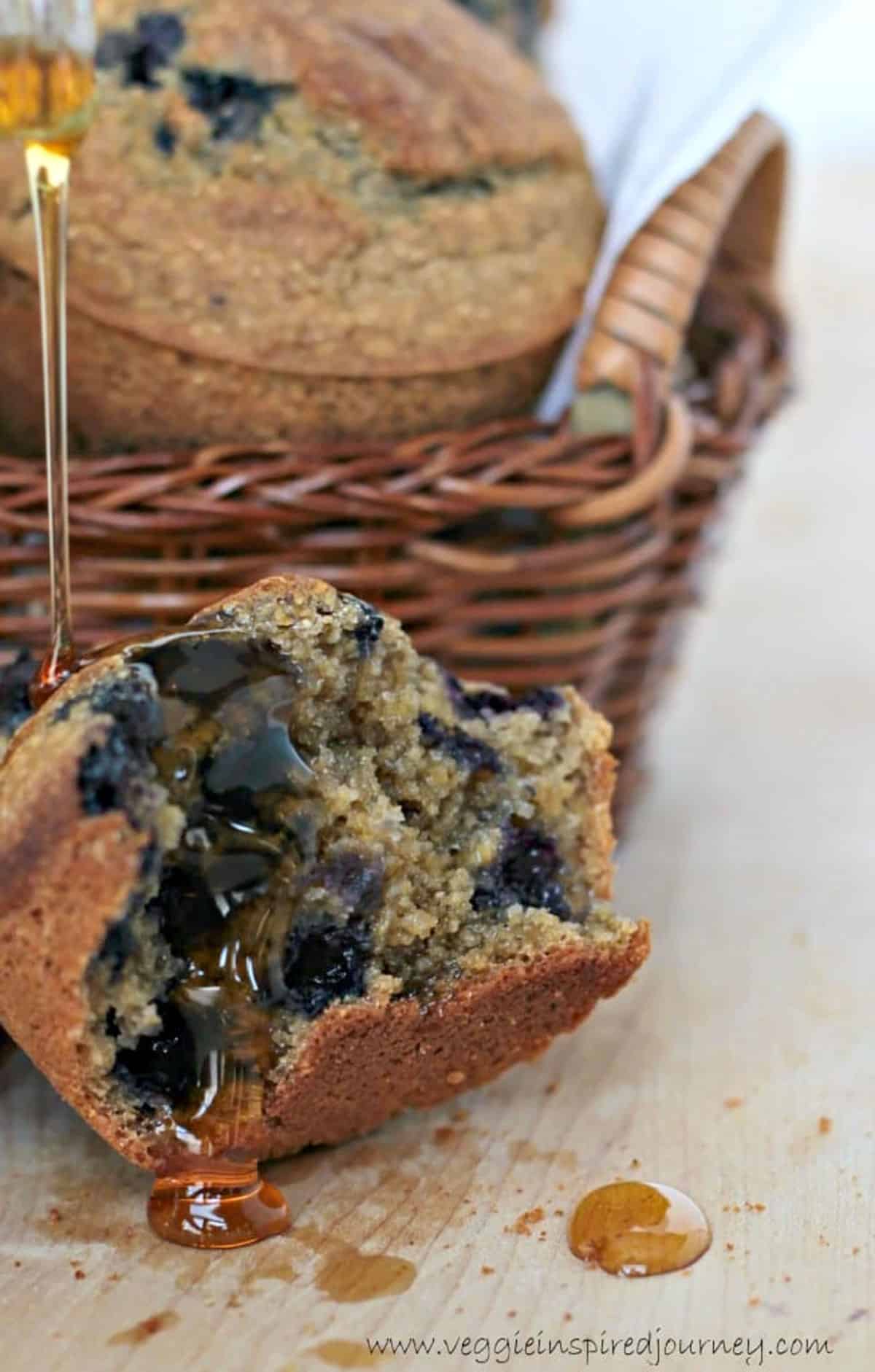 Maple syrup being drizzle over a halved blueberry muffin.