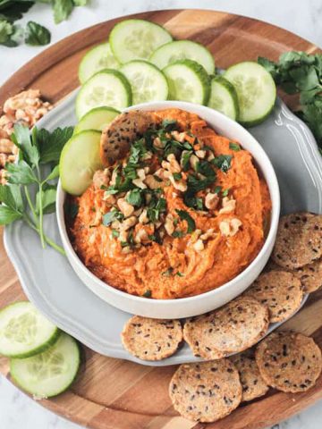 Roasted carrot white bean hummus on a serving tray with cucumbers and crackers.
