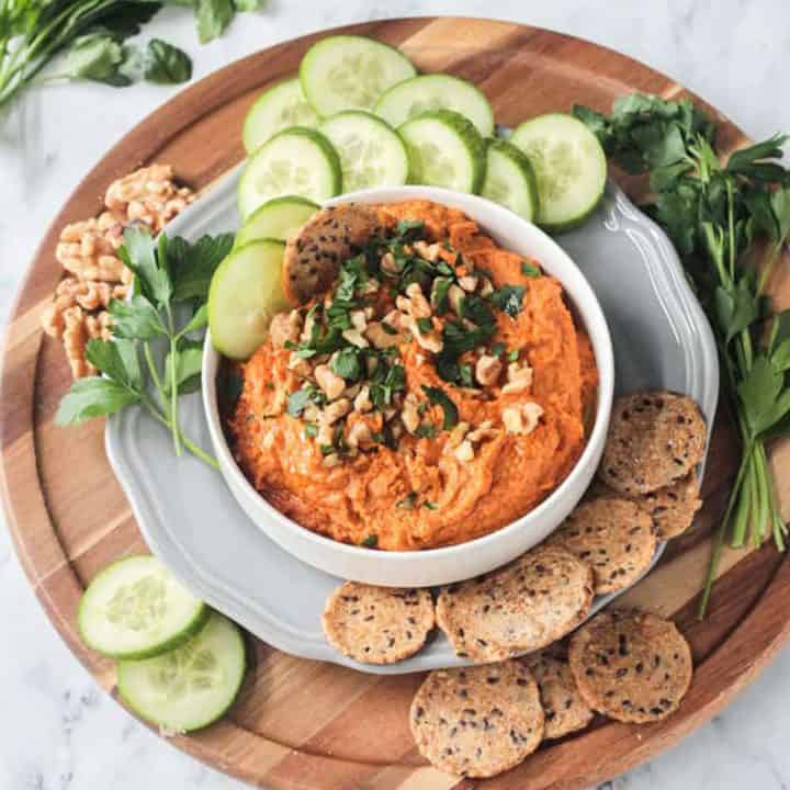 Roasted carrot white bean hummus on a serving tray with cucumbers and crackers.