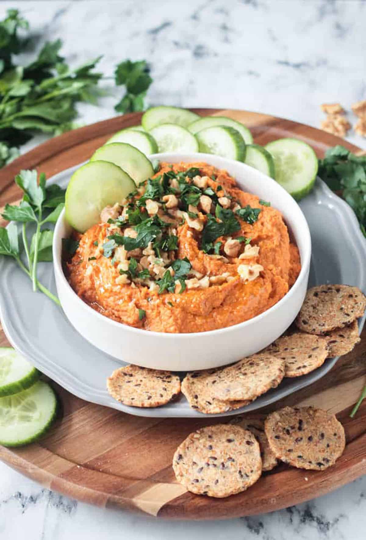 Orange hued dip in a white bowl topped with chopped fresh parsley.