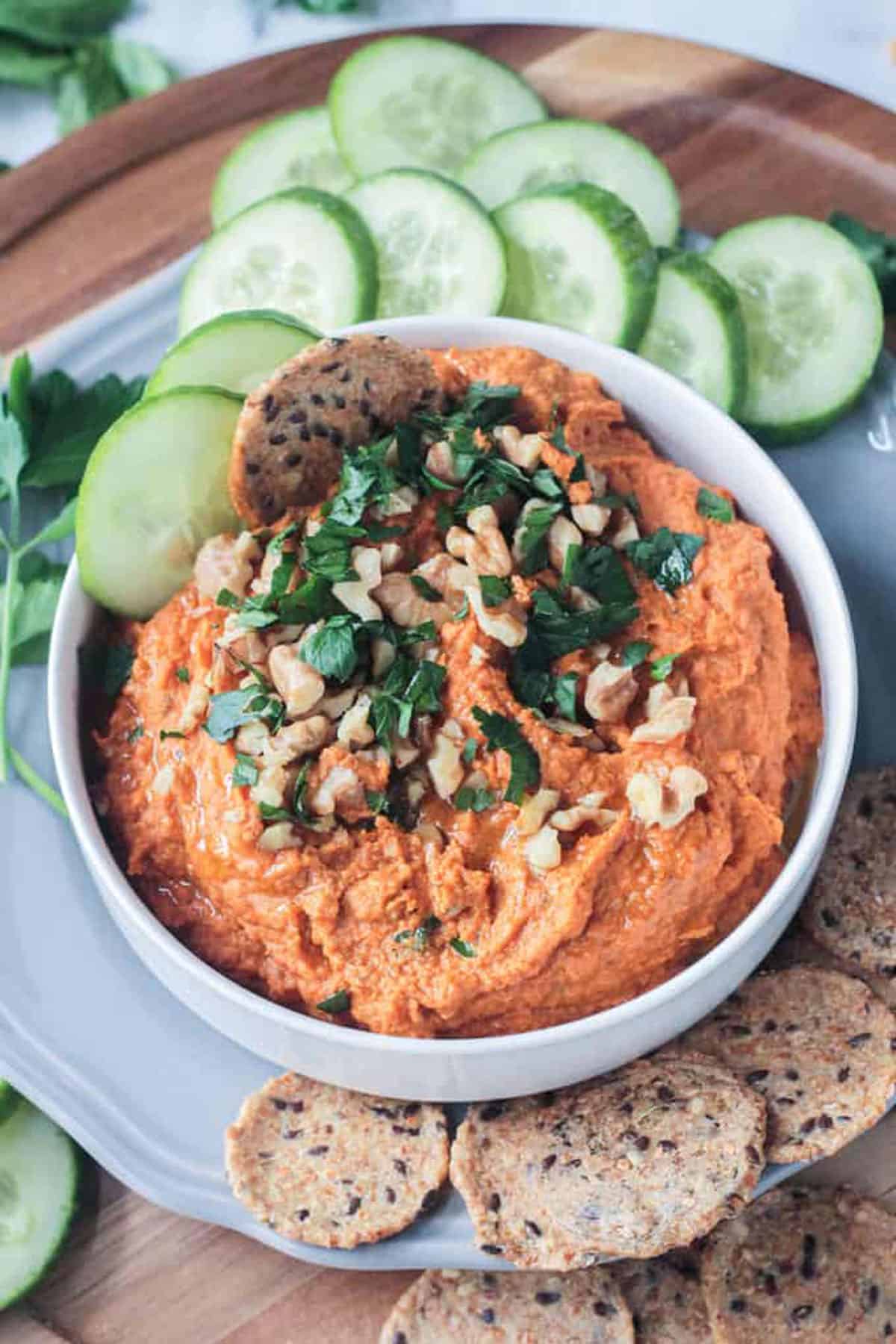 A cracker and 2 cucumber slices in a bowl of carrot hummus.