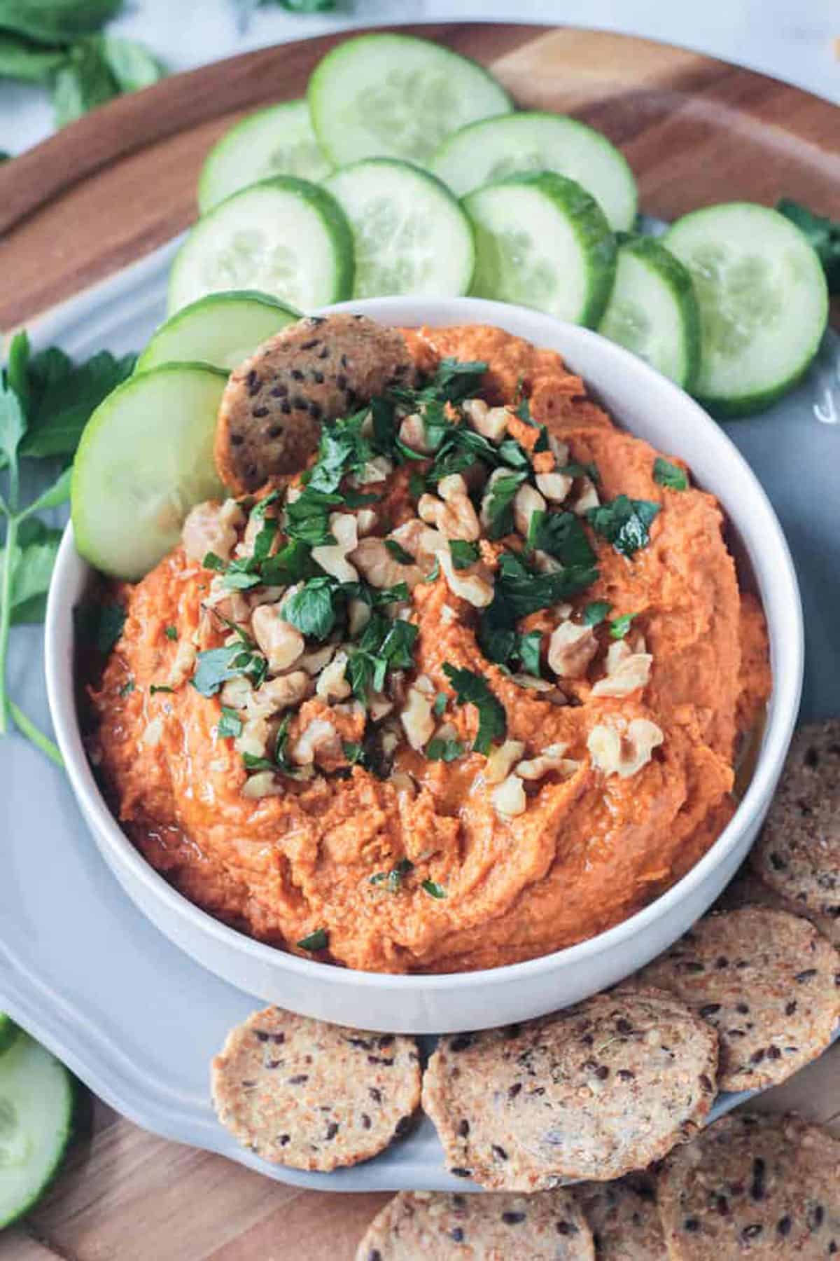 A cracker and 2 cucumber slices in a bowl of carrot hummus.