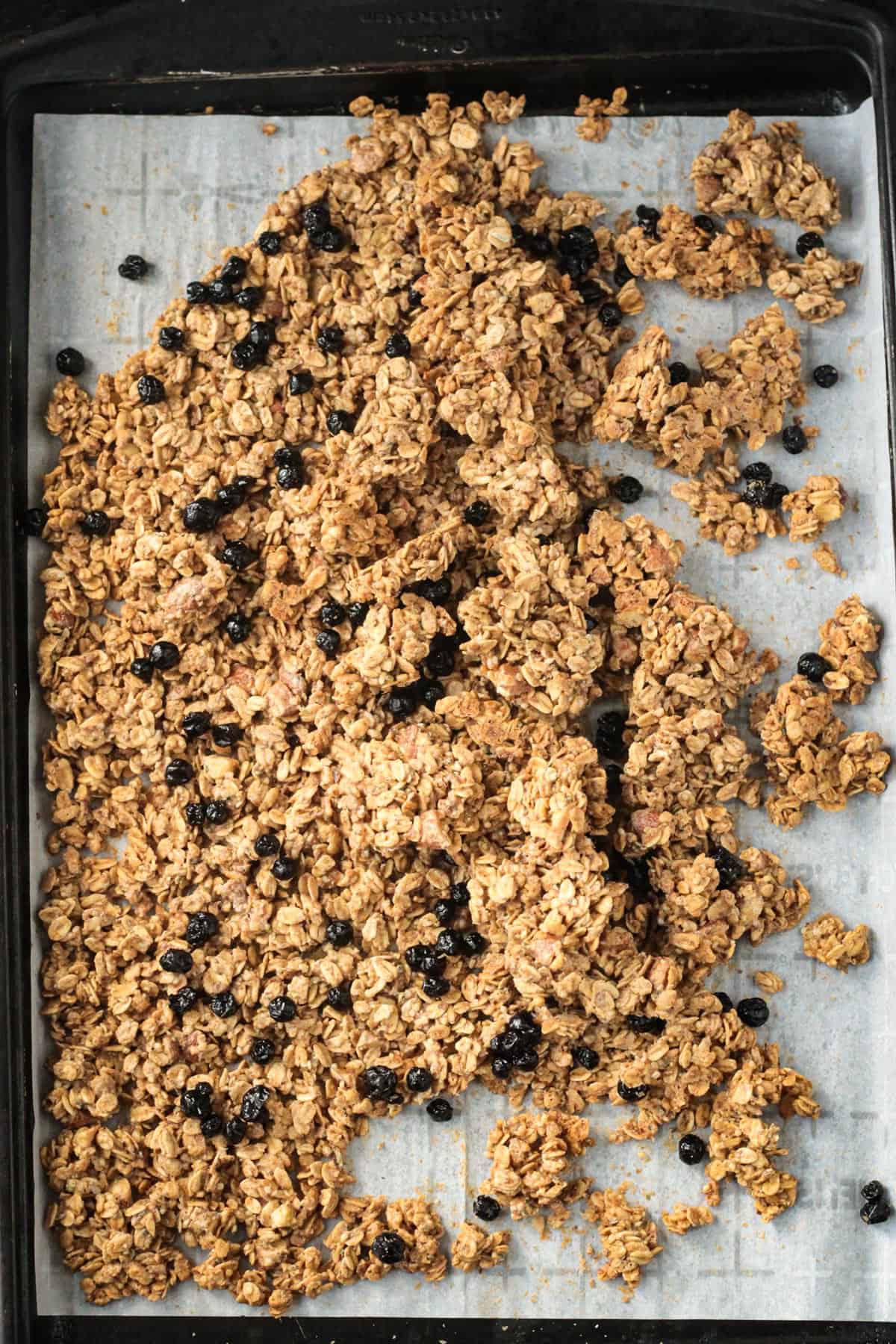 Granola on a baking sheet being broken up in clusters.