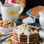 Chopped walnuts on top of white icing that is dripping down the side of a pancake stack.