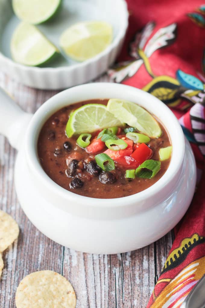 Bowl of Easy Black Bean Soup with a bowl of lime wedges in the background and tortilla chips on the side.