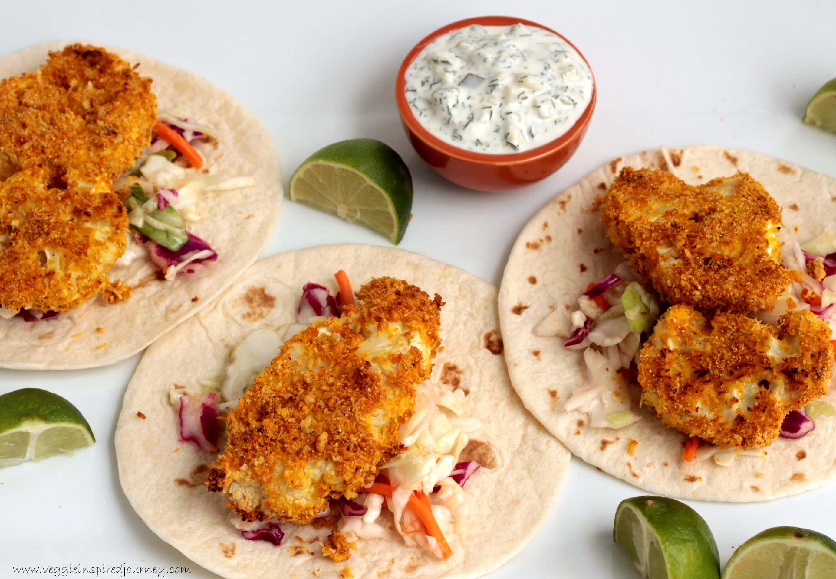 Three cauliflower tacos next to several lime wedges and a small dipping bowl of tartar sauce.