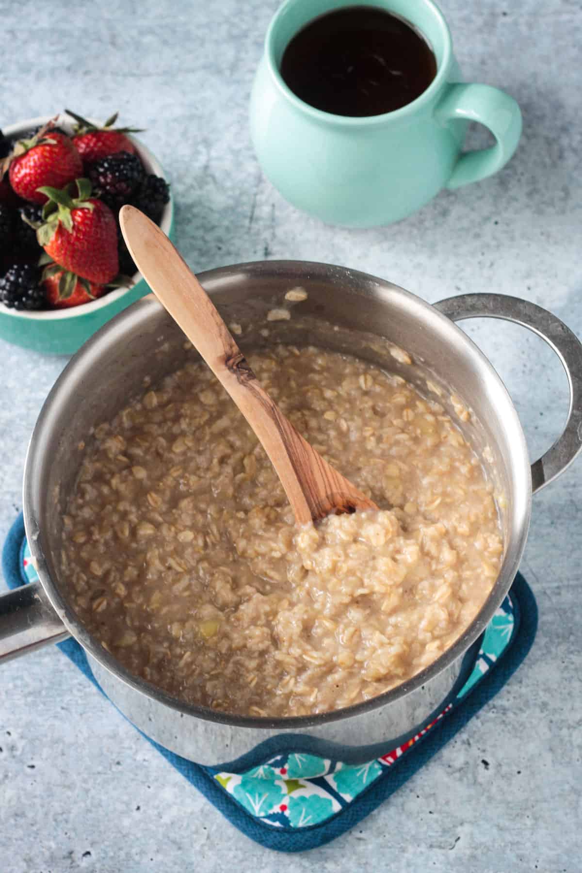 A wooden spoon stirring a pot of creamy oatmeal.