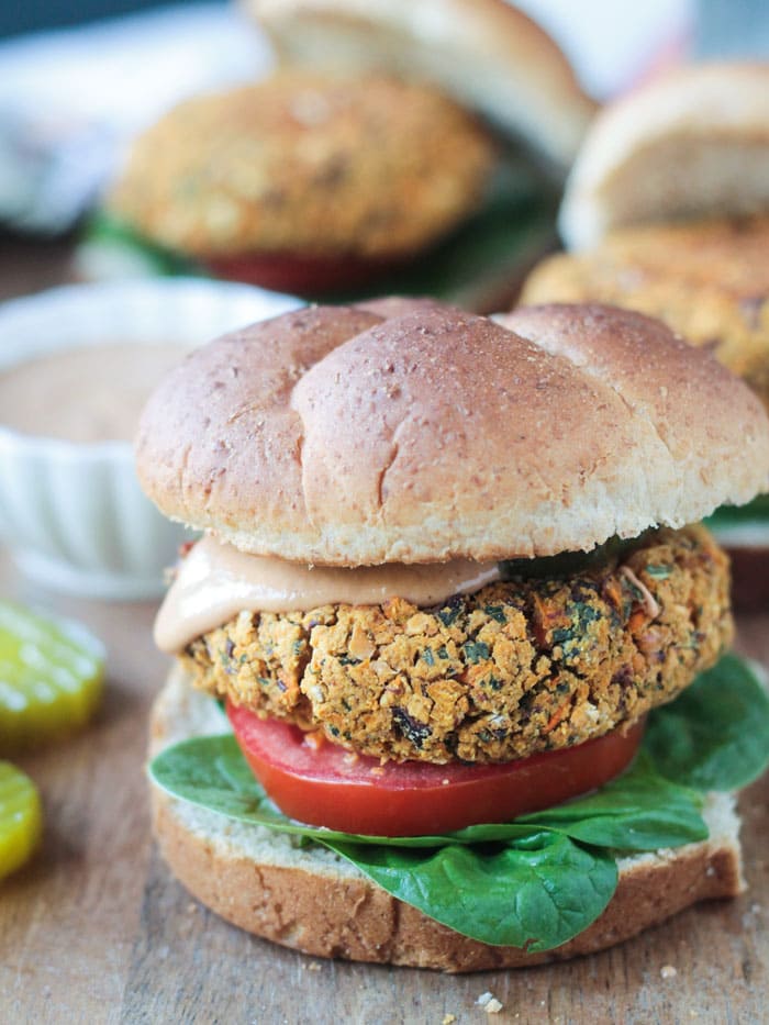 Front view of a Kidney Bean Kale Burger on a wheat bun with spinach, tomato and bbq sauce.