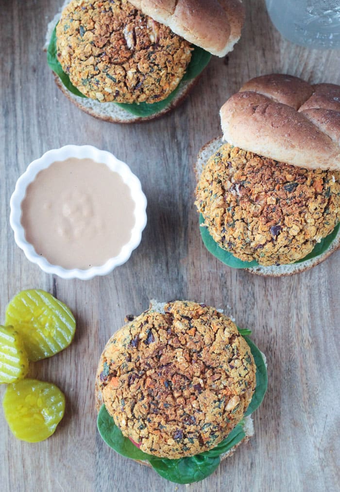 Three veggie burgers, open faced, with spinach leaves underneath. Pickle slices and a small bowl of pickle slices next to them.