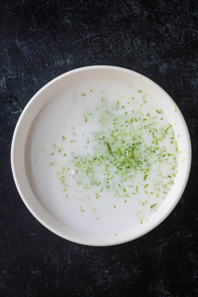 Lime zest added to coconut milk in a bowl.