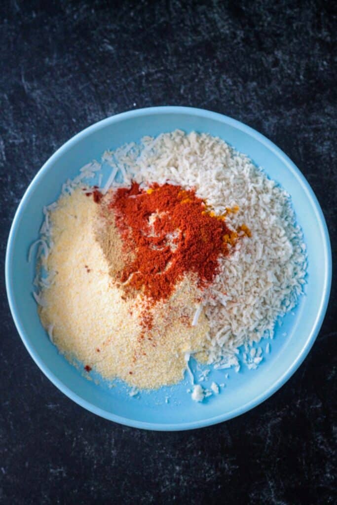 Cornmeal. breadcrumbs, shredded coconut, and spices in a bowl.
