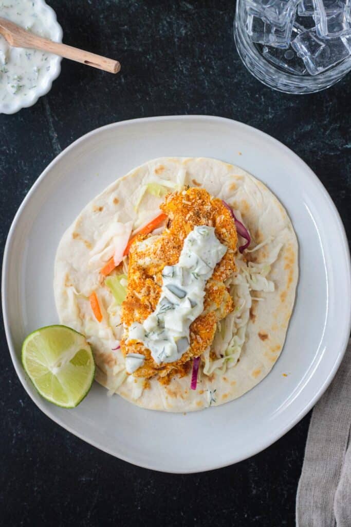 A tortilla filled with coleslaw, breaded roasted cauliflower, and topped with tartar sauce.