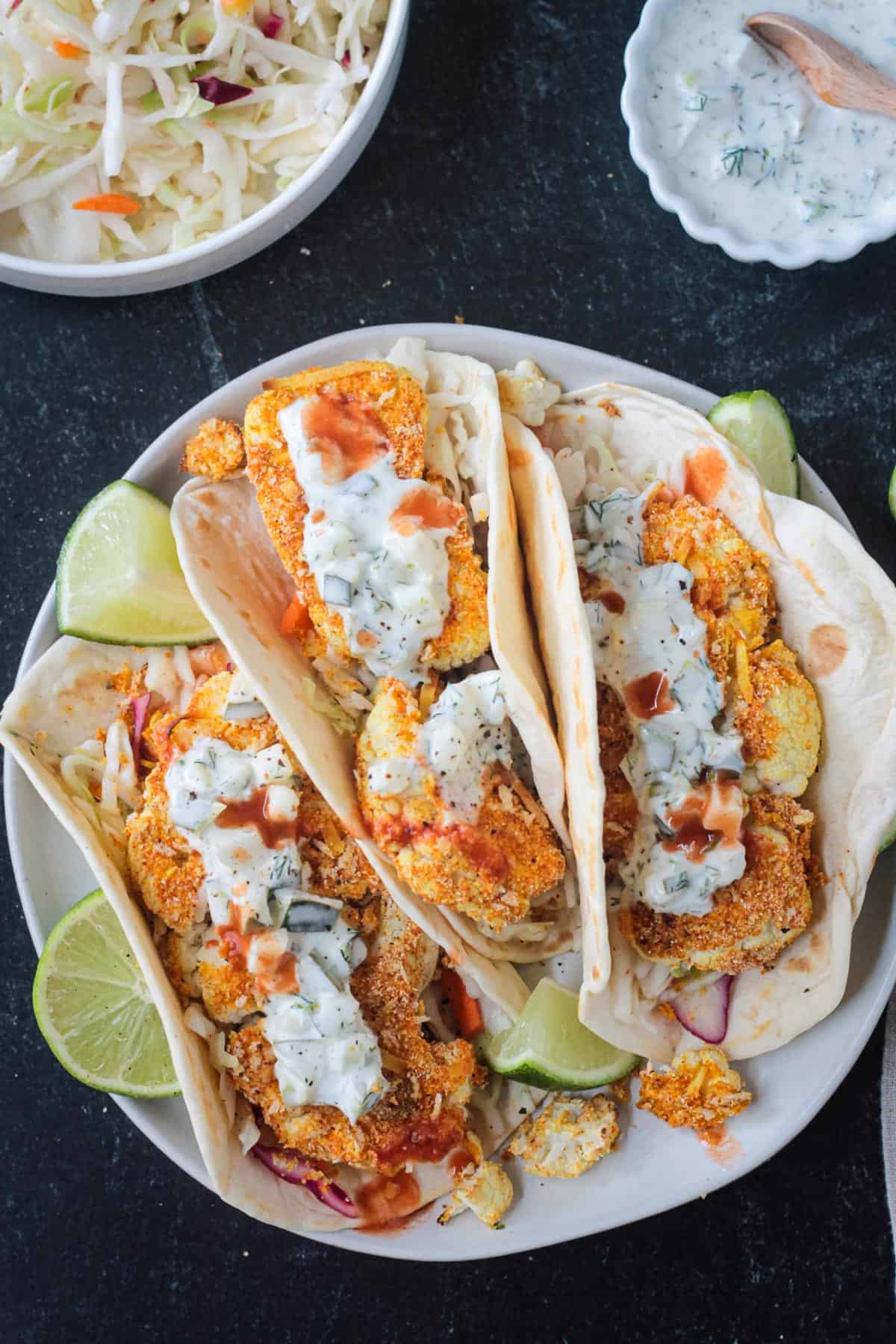 Overhead view of three folded cauliflower tacos on a plate with sauce.