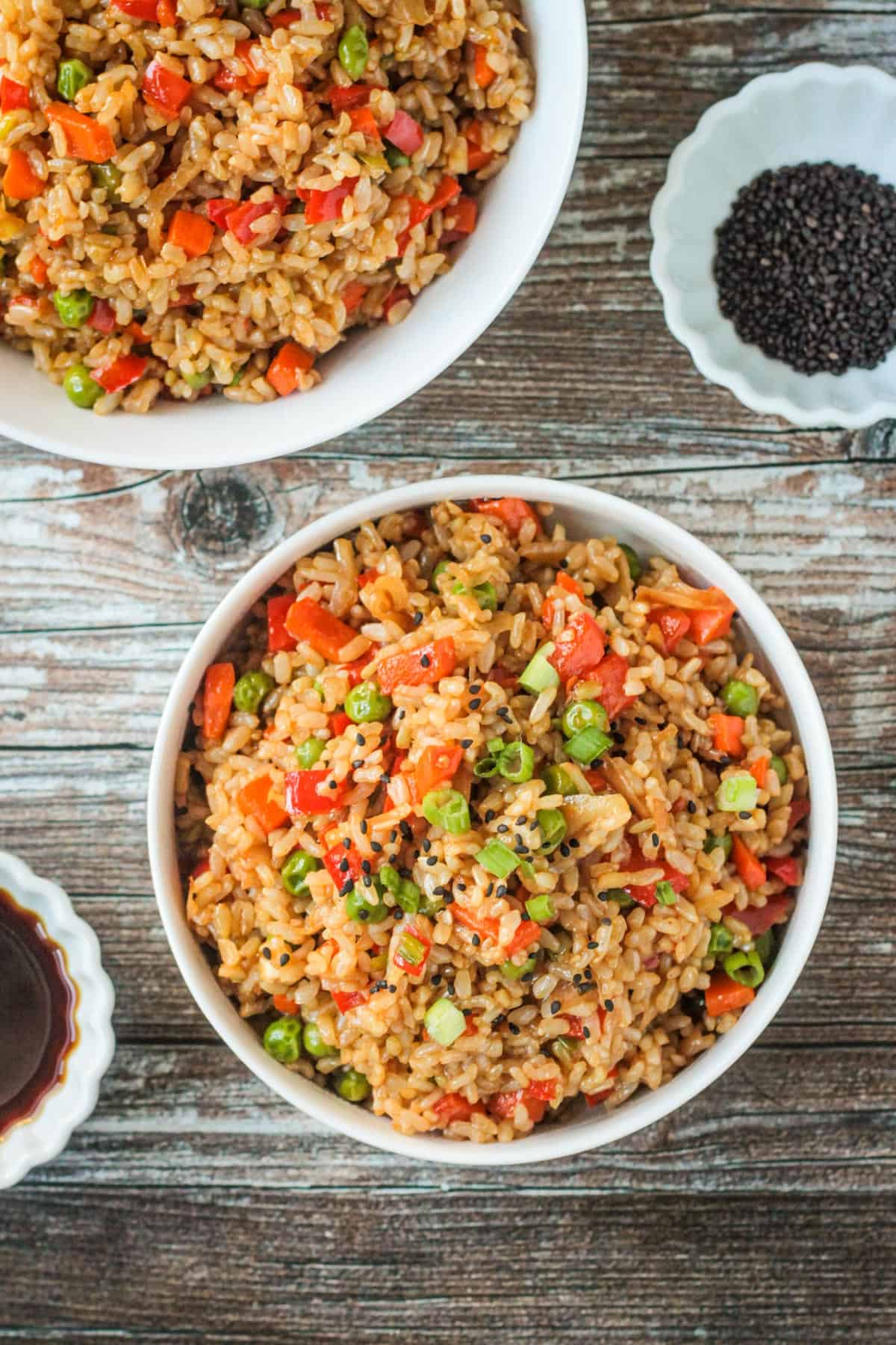 Bowl of vegan fried rice next to small bowls of soy sauce and black sesame seeds.