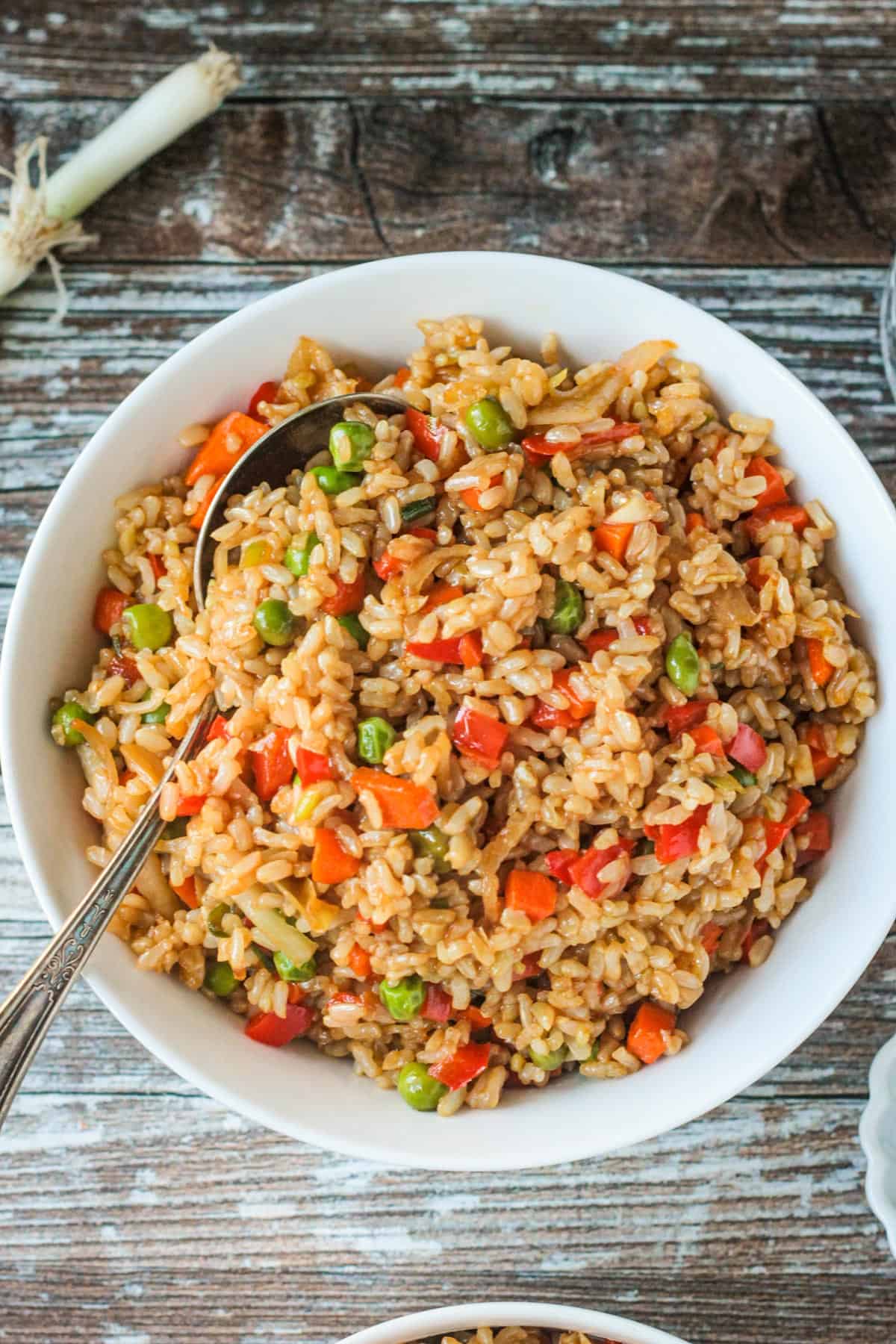 Metal spoon in a serving bowl of vegetable fried rice.