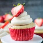 Close up of one vanilla frosted strawberry cupcake in a red paper liner.