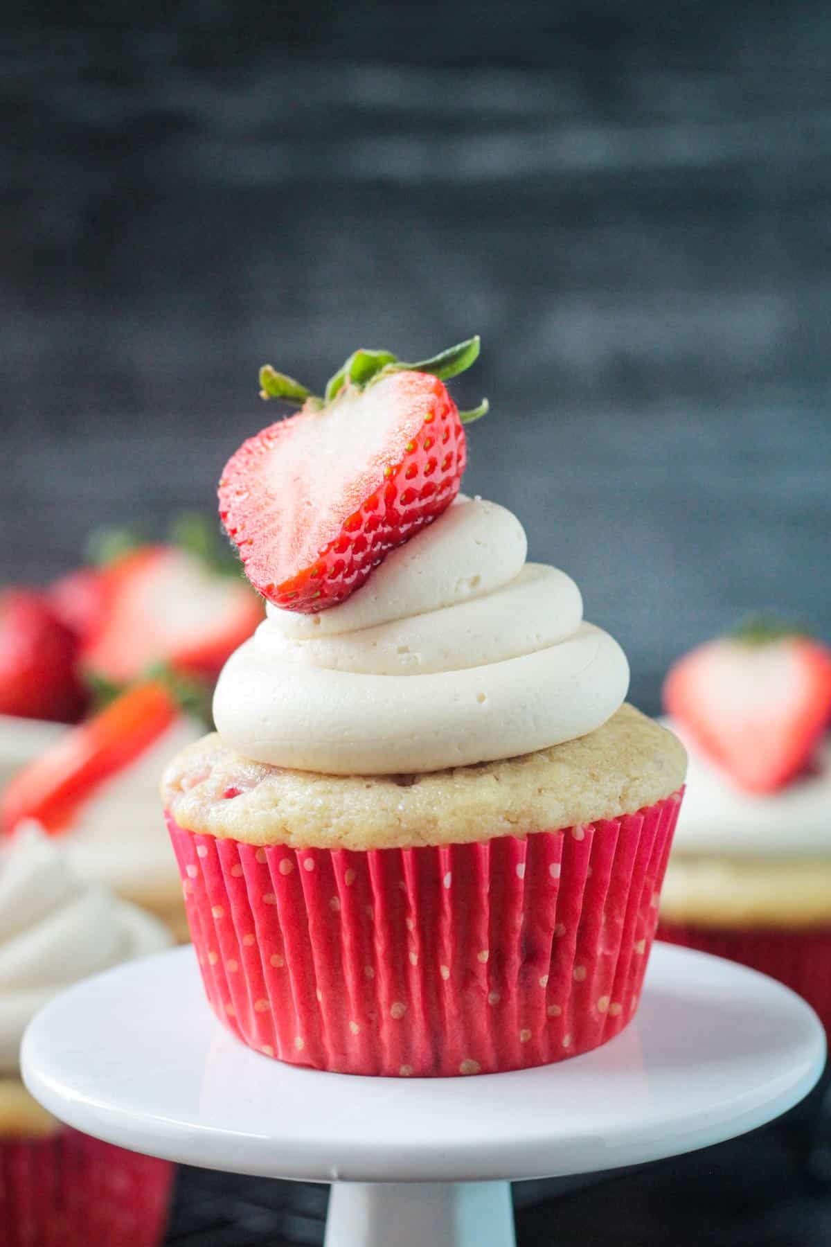 Close up of one vanilla frosted strawberry cupcake in a red paper liner.