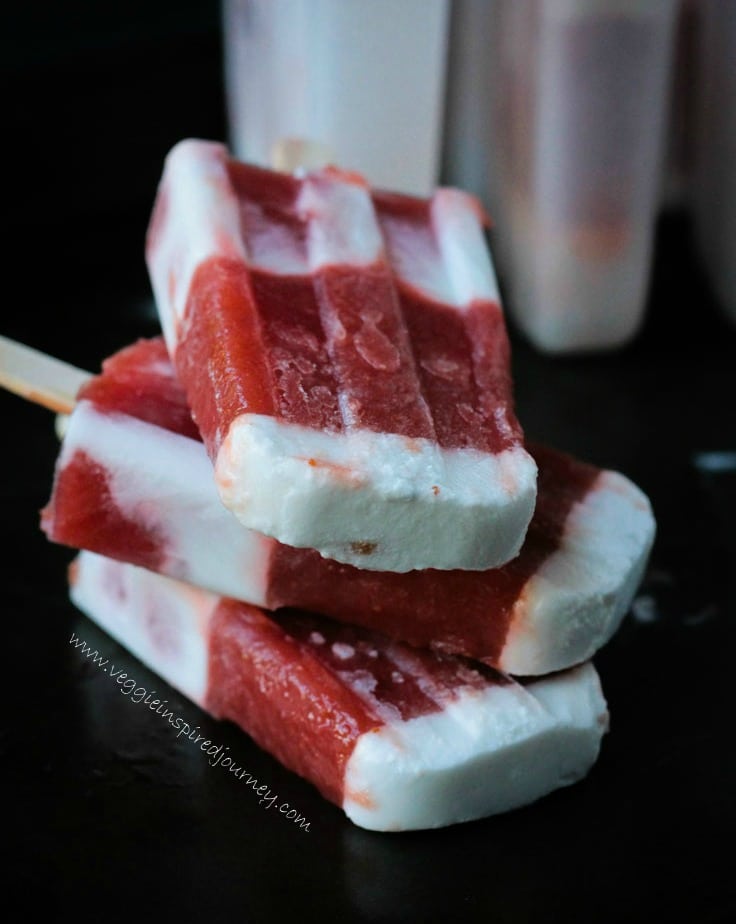 A stack of three Strawberry Rhubarb Coconut Milk Popsicles on a black tray.
