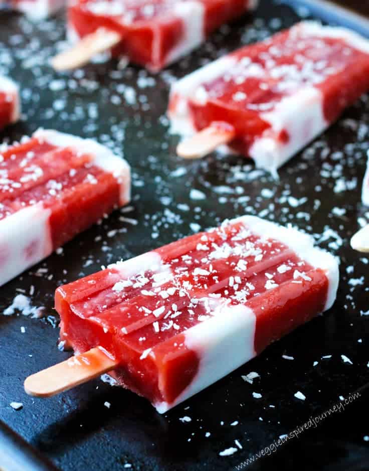 Strawberry Rhubarb Coconut Milk Popsicles laid out flat on a black tray and sprinkled with shredded coconut.