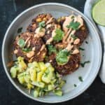 Four black bean patties on a plate with pineapple avocado salsa and chipotle crema.