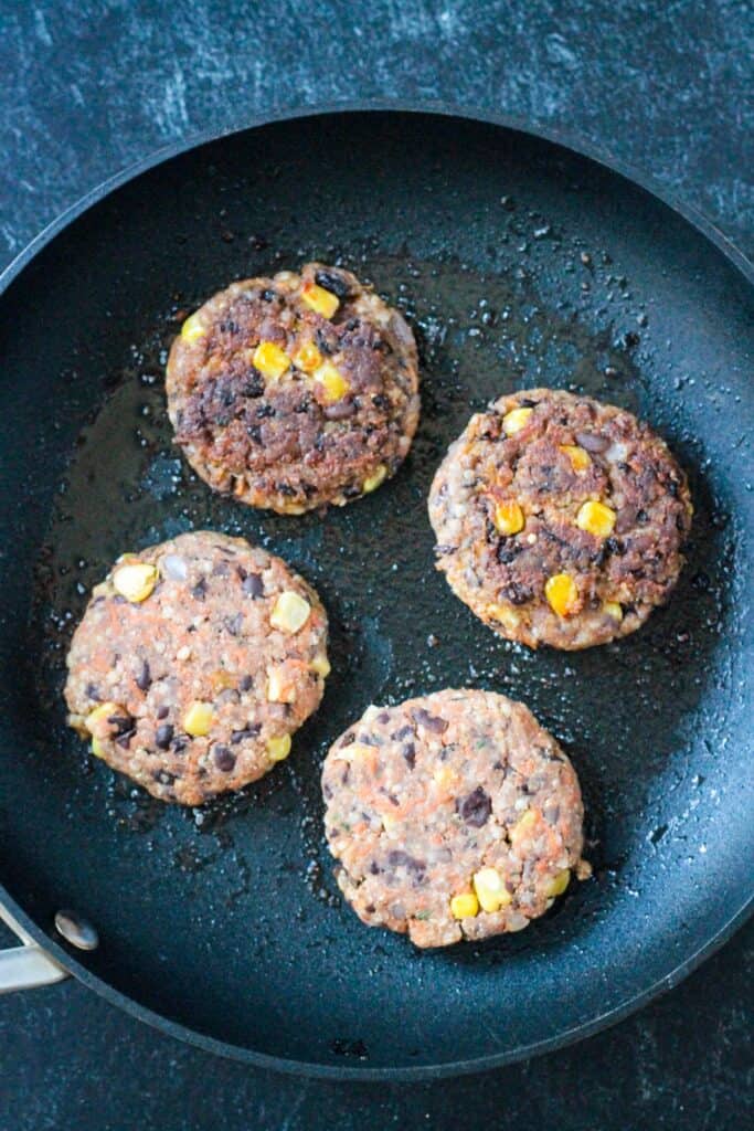 Four bean patties cooking in a skillet.