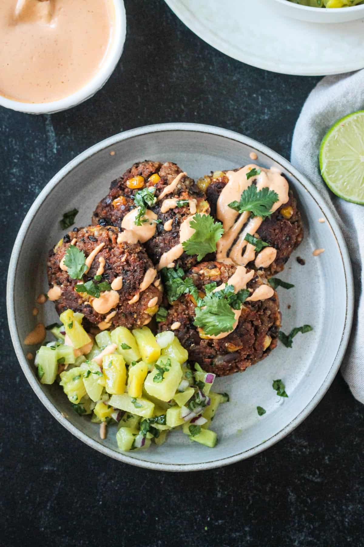 Four black bean patties on a plate with pineapple avocado salsa and chipotle crema.
