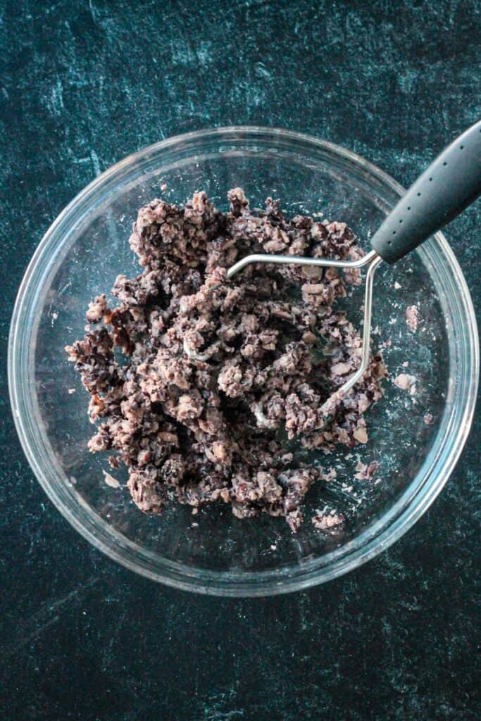 Black beans smashed in a bowl with a potato masher.